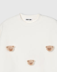Close-up of plush teddy bear face with check ears on cream cotton showing tonal layered texture