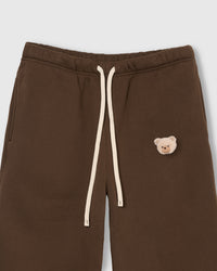 Close-up of check-ear plush teddy bear face on brown cotton sweatpant showing gingham ear detail