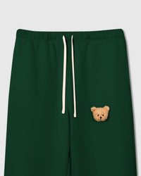 Close-up of elastic waistband and plush teddy bear face applique on green 350gsm cotton showing cream drawstring and sherpa texture