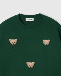 Close-up of plush bear face appliques on green 230gsm cotton showing fuzzy 3D texture and embroidered features