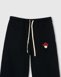 Close-up of plush mushroom applique with red cap, white polka dots, and cream stem on black premium cotton