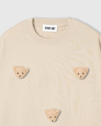 Close-up of plush bear face appliques on beige 230gsm cotton showing fuzzy 3D texture and embroidered features