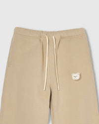 Close-up of check-ear plush teddy bear face on beige cotton sweatpant showing gingham ear detail