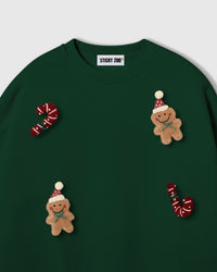 Close-up of scattered plush appliques on forest green sweatshirt showing gingerbread men and candy cane detail