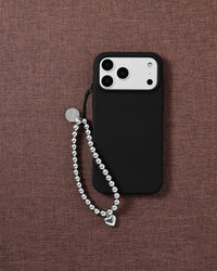 STICKYZOO beaded phone strap draped beside a black phone case on woven mauve fabric, silver ball beads ending in a puffy heart drop