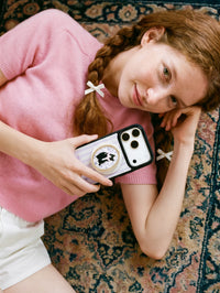 Framed tuxedo cat phone case held on a vintage rug with the oval cat medallion on the back in soft daylight