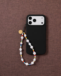 STICKYZOO pearl phone strap looped onto a black phone case on woven brown fabric, gold disc showing.