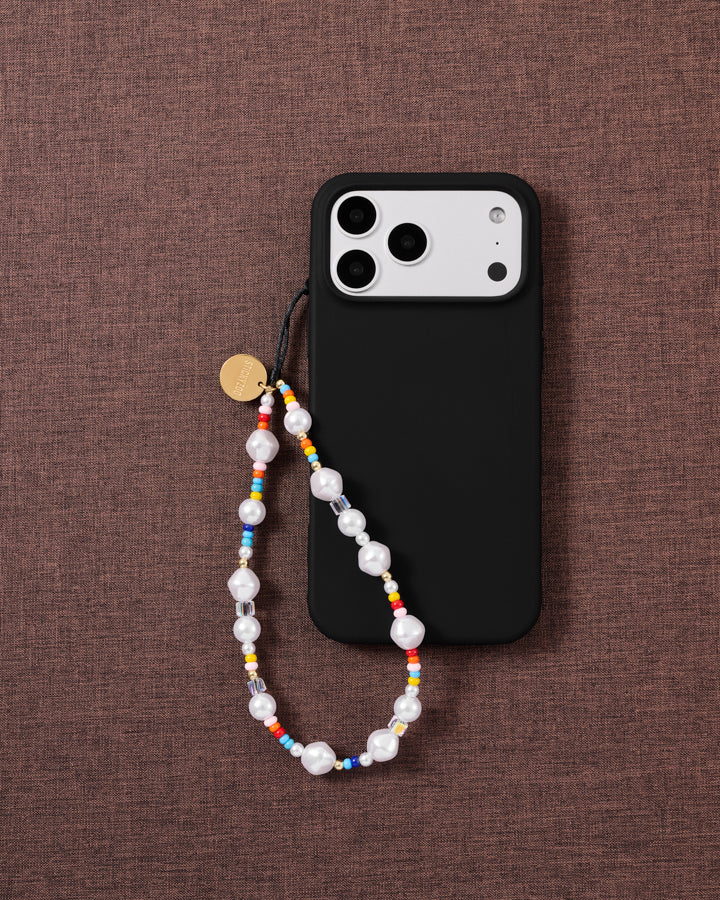 STICKYZOO pearl phone strap looped onto a black phone case on woven brown fabric, gold disc showing.