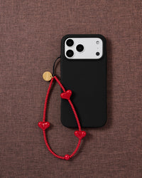Red heart bead phone strap on a black phone case, worn hands-free from the wrist
