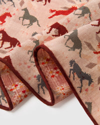 Close-up of the hand-illustrated galloping horses in red, burgundy, and grey on the blush silk field