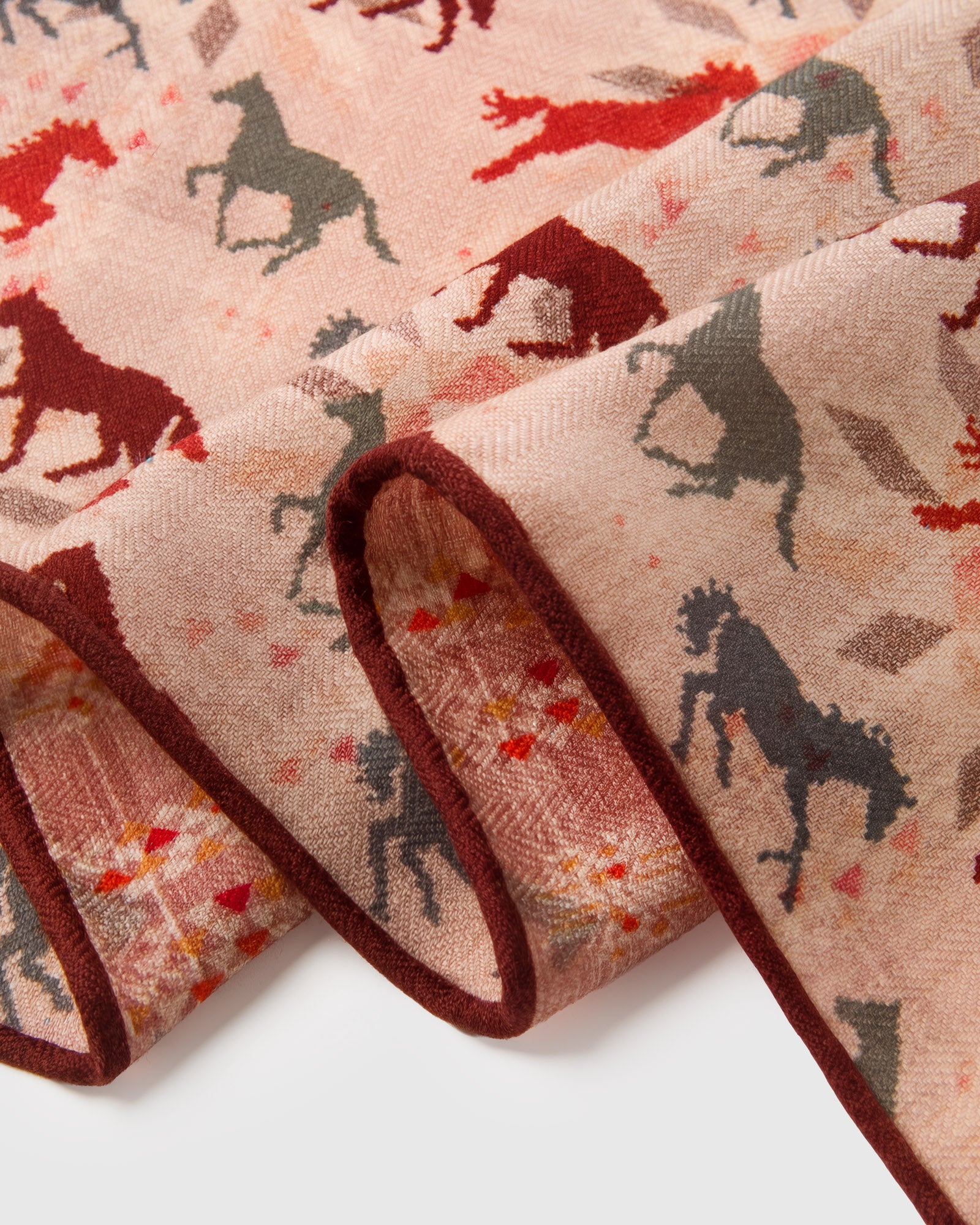 Close-up of the hand-illustrated galloping horses in red, burgundy, and grey on the blush silk field