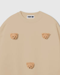 Detail of scattered bear faces on STICKYZOO cream sweatshirt showing handmade dimensional craft