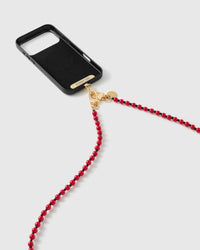 Close-up of the gold-tone dual clasp and engraved tag connecting the scarlet beaded strap to a black phone case on a white background.