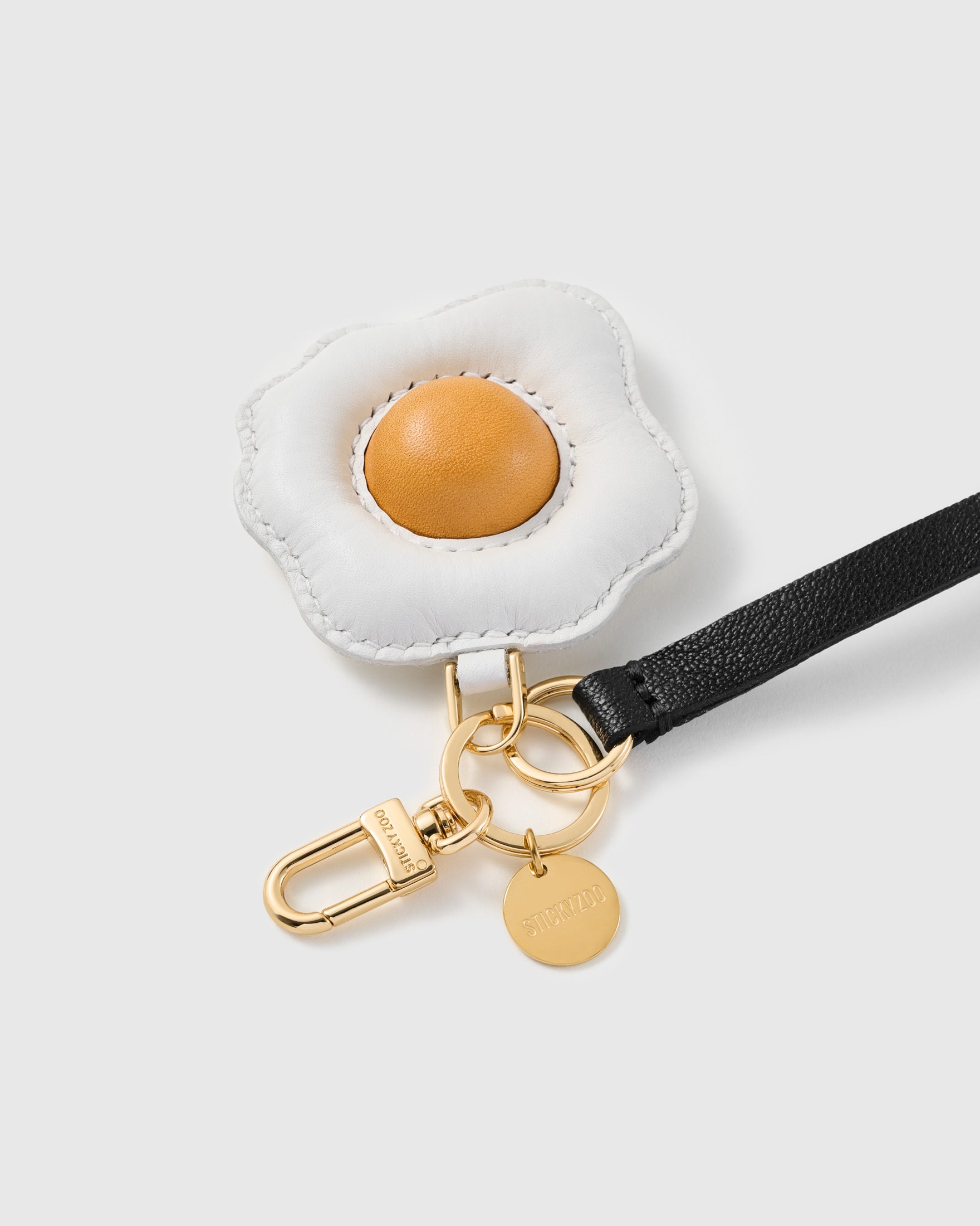 Close-up of the hand whip-stitched leather fried-egg charm and engraved STICKYZOO gold hardware