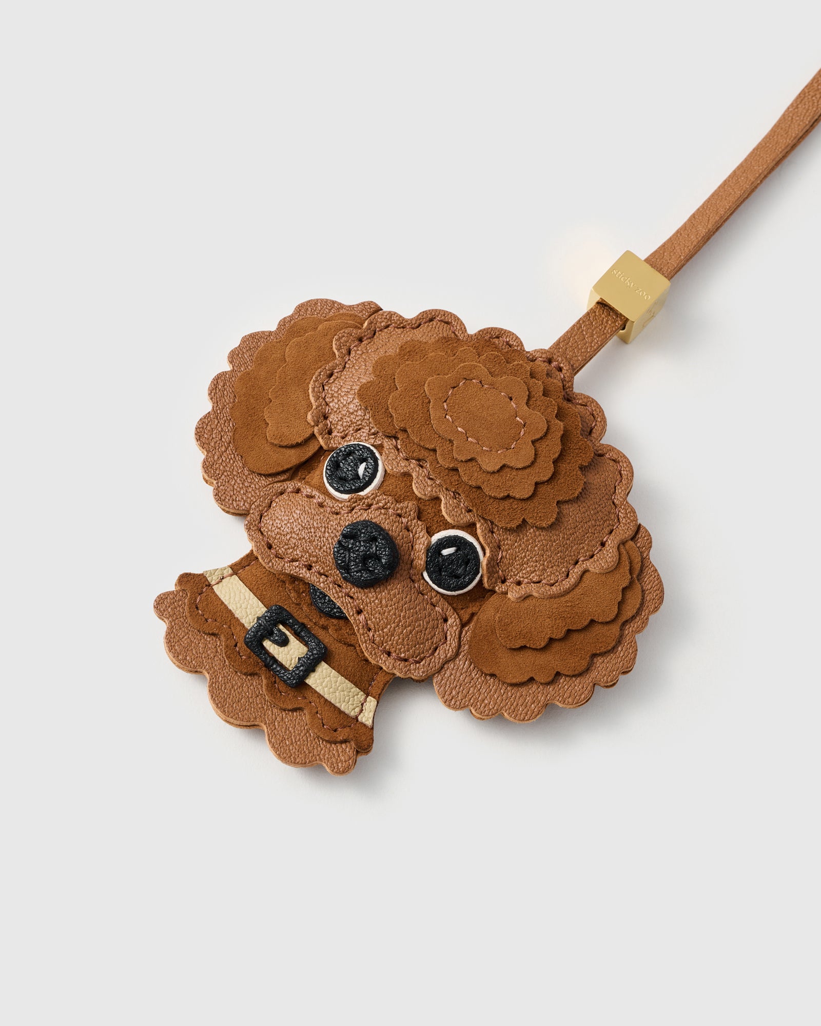{{7 days. One pair of hands.}} Close-up of The Poodle Charm — every scalloped Alcantara curl individually hand-cut and layered over French Alran goatskin. Gold collar, deep black eyes. Seven days of craft per piece.
