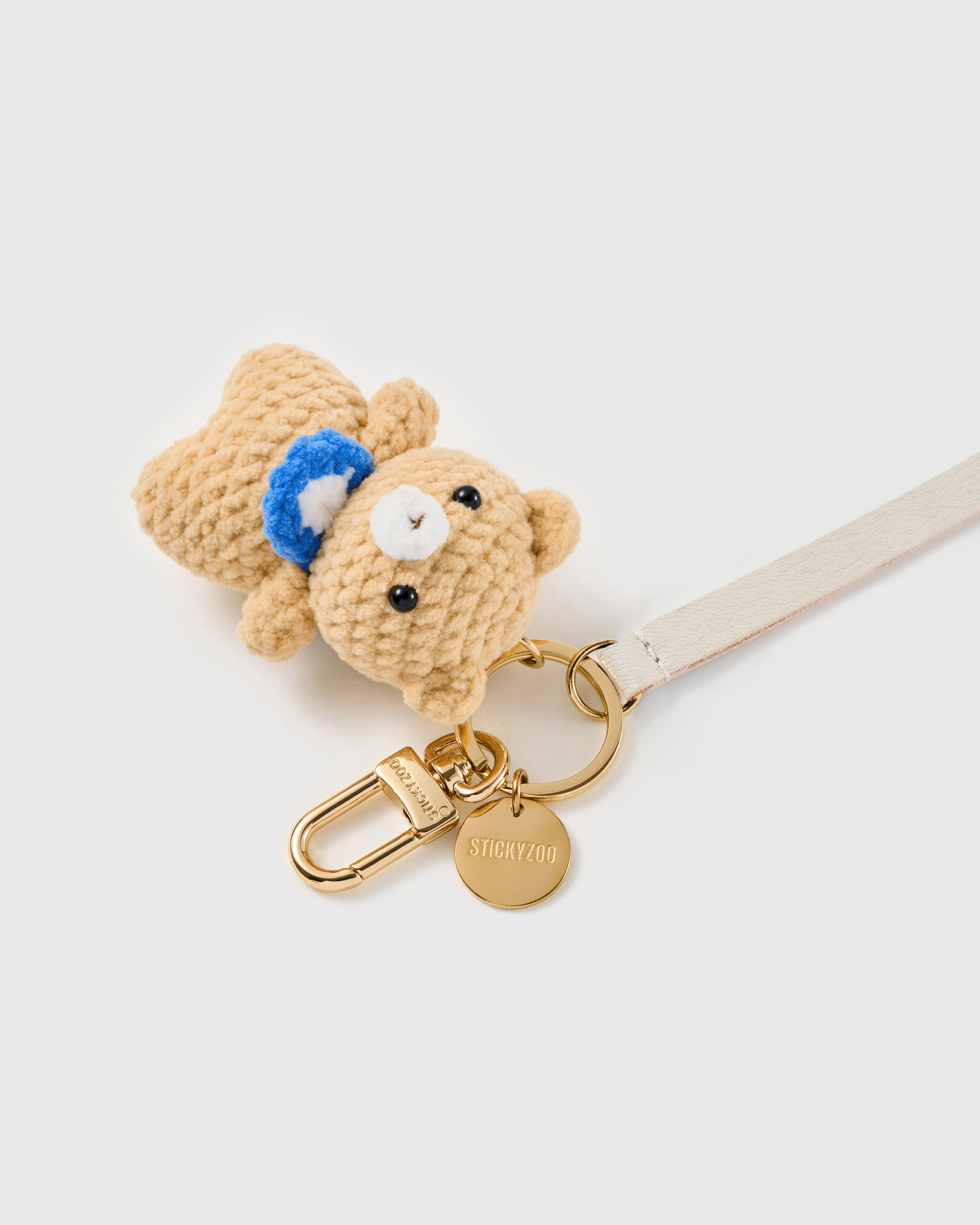 Tiny teddy leather phone strap in ivory clipped to a phone case showing the hands-free wrist loop in use