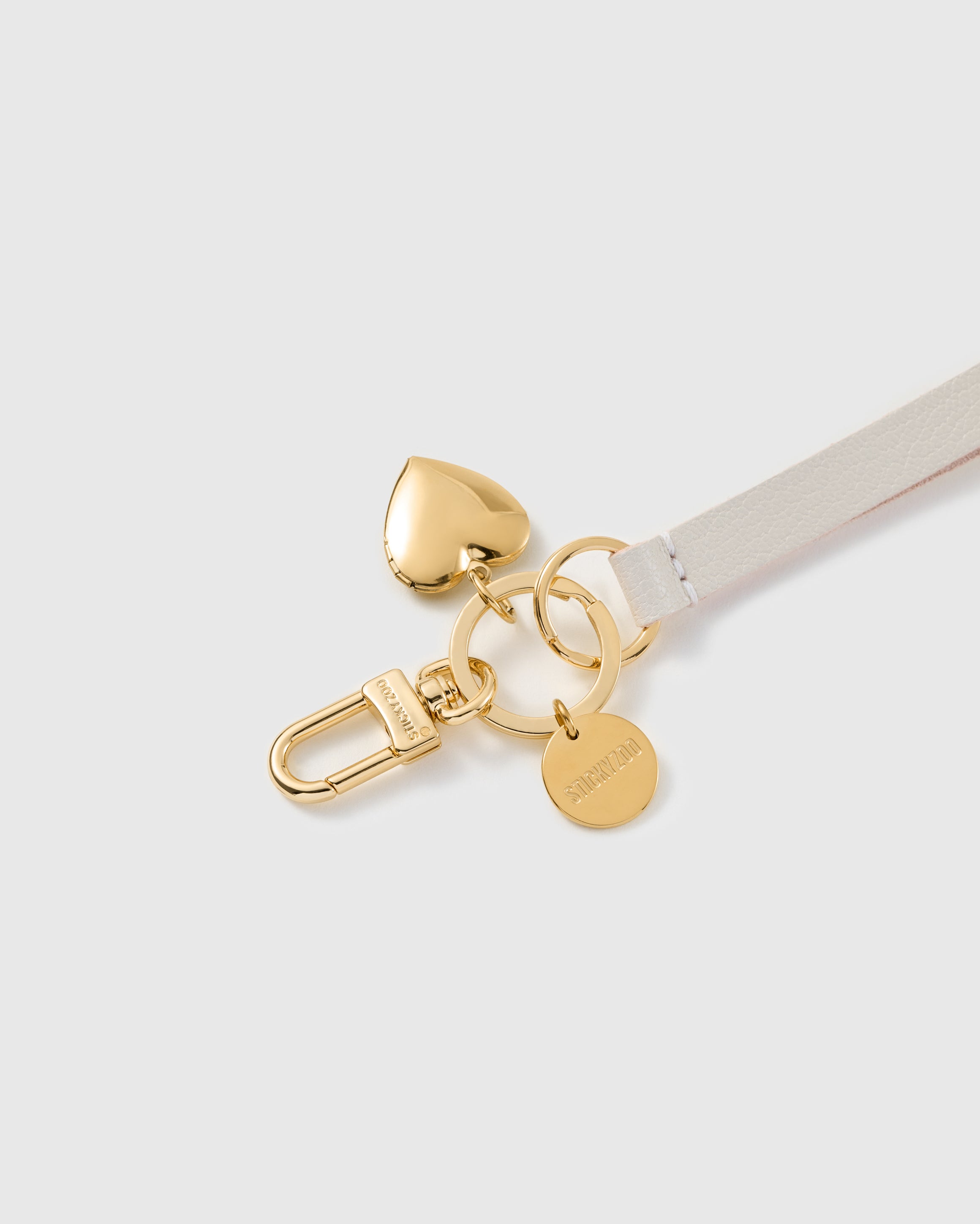 Golden heart leather phone strap close-up — sculpted gold-plated puffed heart charm and STICKYZOO engraved hook