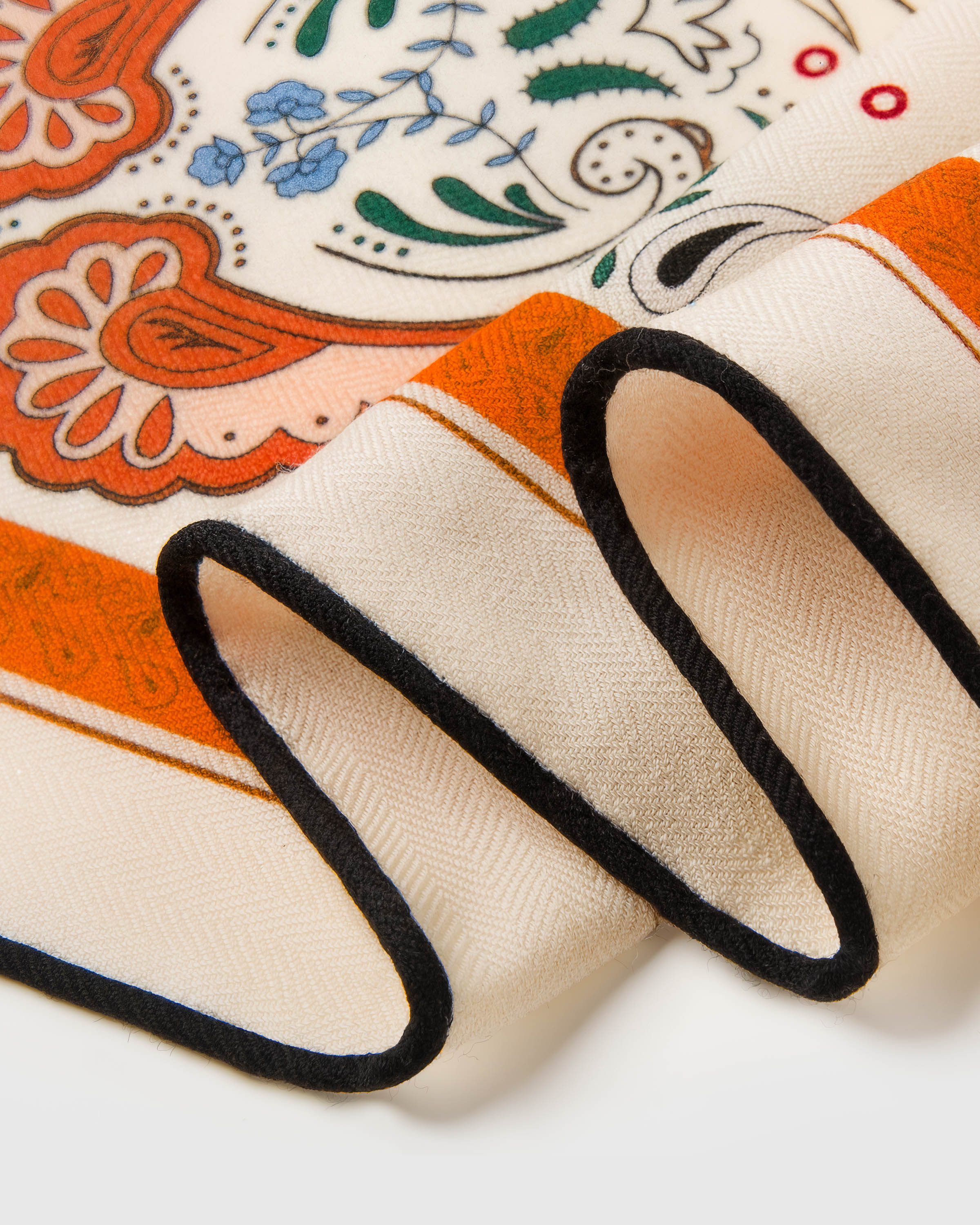 Close-up of the hand-illustrated rust paisley border meeting the cream field on pure silk