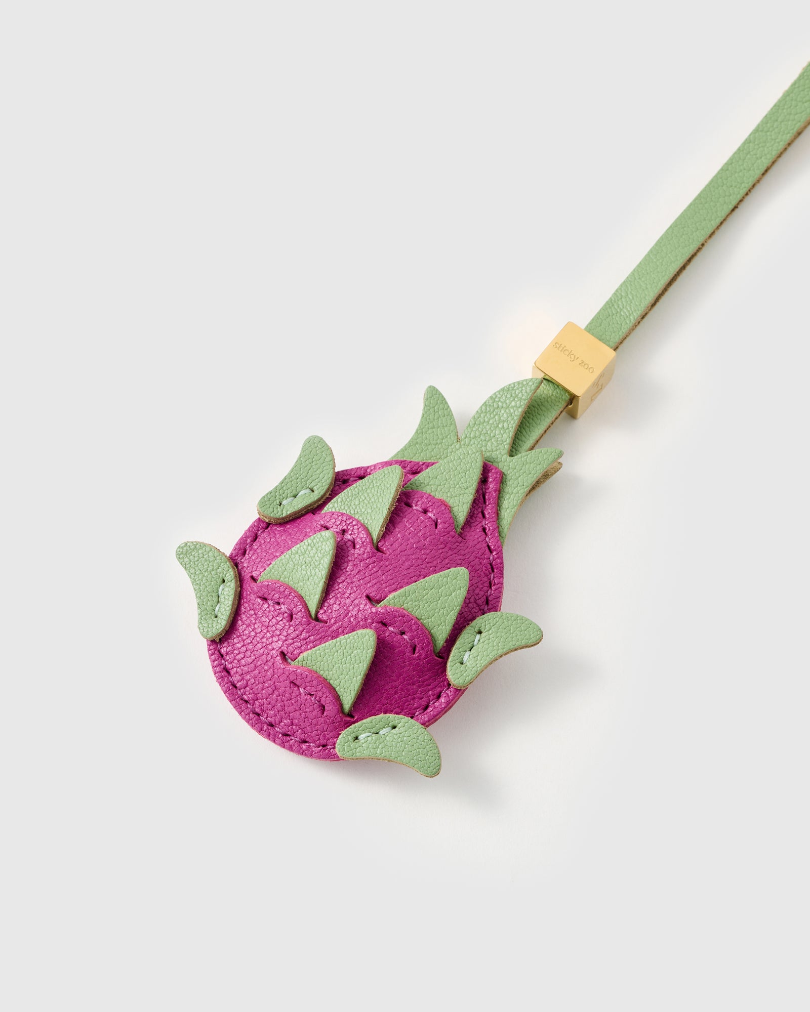 Back of the STICKYZOO pitaya charm showing magenta French Alran leather body with layered green leather scales and engraved gold cube