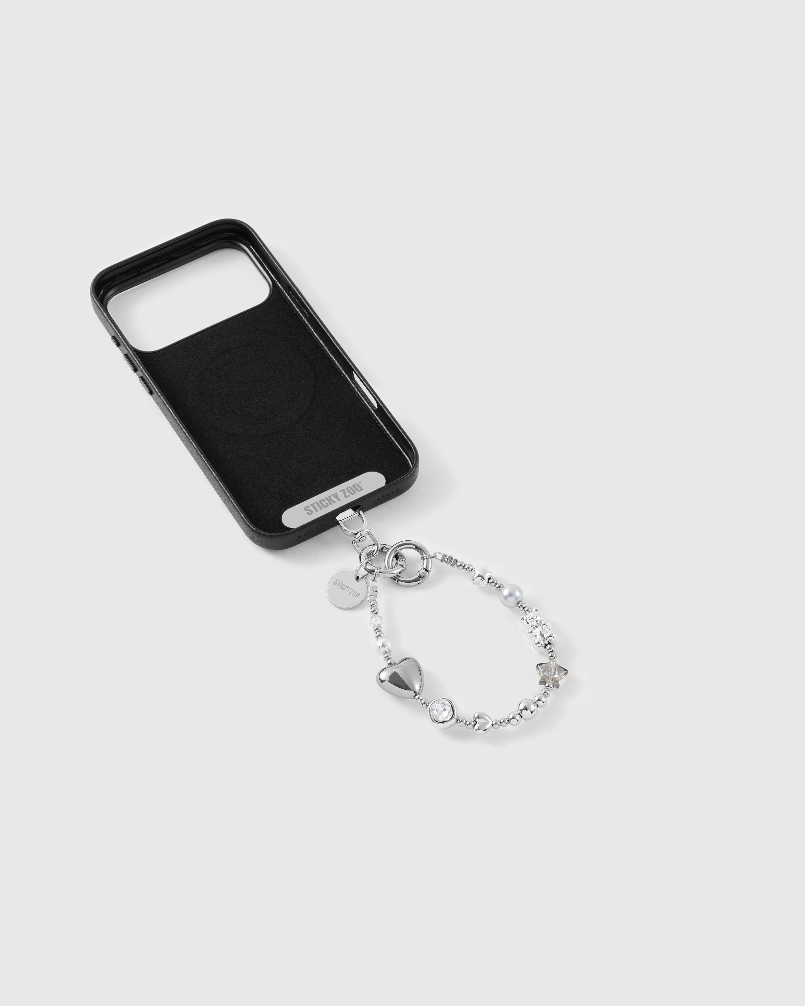 Silver beaded wrist strap clipped to a black phone case, silver puff heart, faceted clear bead, grey pearl-effect bead and STICKYZOO disc