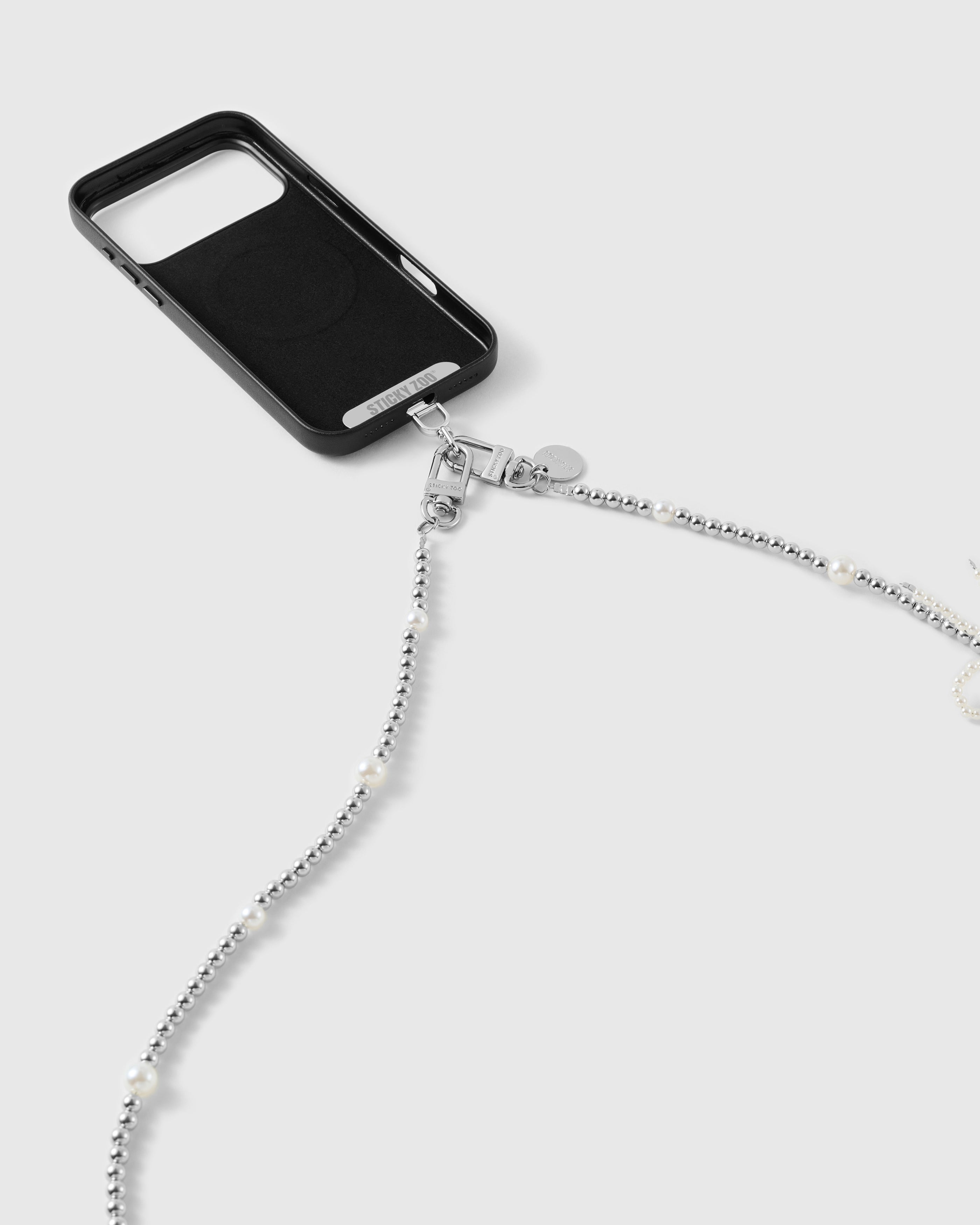 Silver-tone dual clasp and engraved disc joining the beaded strand to a black phone case, faux-pearls spaced along the beads.