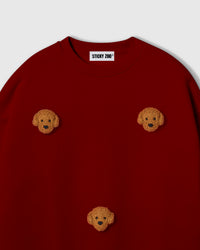 Close-up of plush poodle face on burgundy cotton showing curly golden textured fur and embroidered features