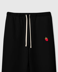 Close-up of hand-stitched plush strawberry with red body, white seeds, and green stem on black cotton