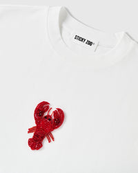 Detail of the beaded lobster applique beside the ribbed crew neck and STICKYZOO neck label, showing raised glass-bead and sequin texture.