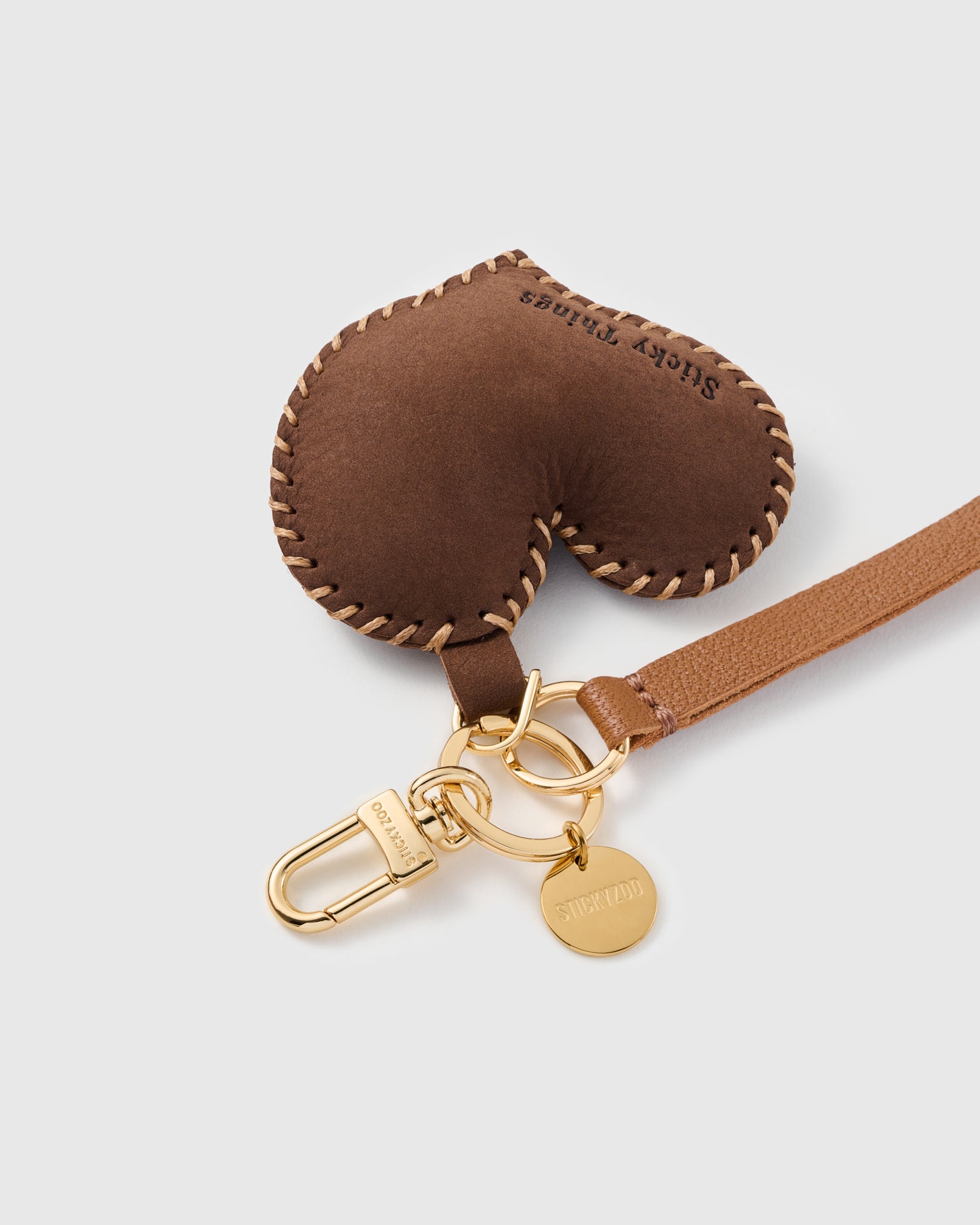 Close-up of the hand whip-stitched cocoa leather heart and engraved STICKYZOO gold hardware