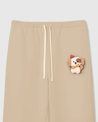 Close-up of plush puppy applique on cream cotton sweatpant showing 3D texture, red beret, and orange scarf detail