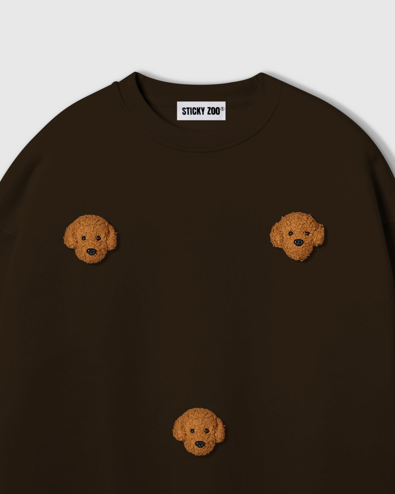 {{Not printed — stitched}} Close-up of plush poodle face applique on dark brown cotton showing golden curly fur texture