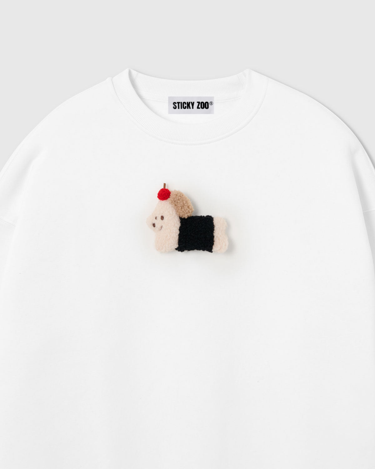 {{Not printed — stitched}} Close-up of hand-stitched plush dachshund in black coat with red apple on white cotton sweatshirt showing 3D texture