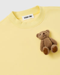 Detail of single plush teddy bear on lemon fleece showing embroidered features and collar