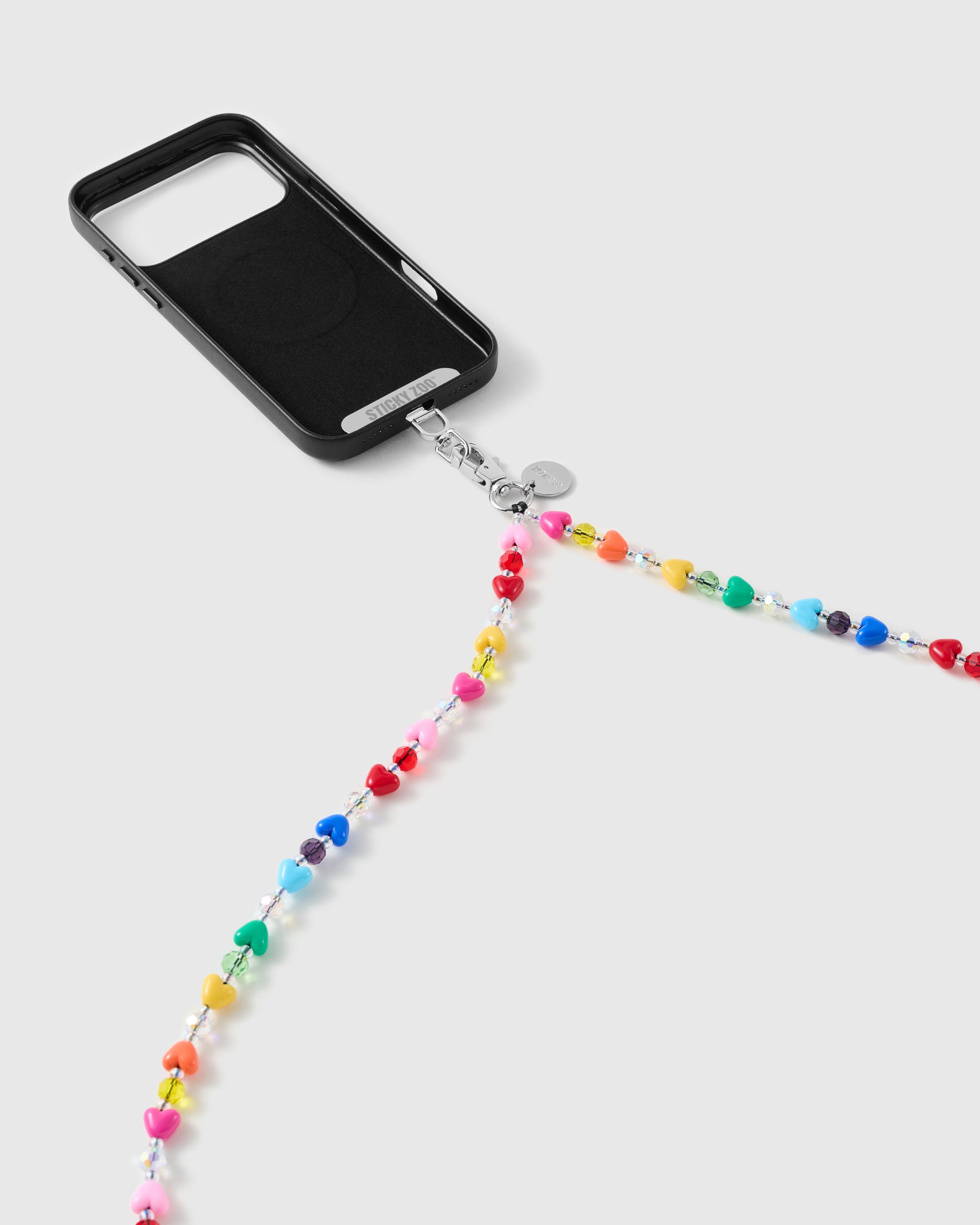Black phone case with the multicolour heart-bead strap draping from a silver-tone clasp and engraved disc against a soft grey backdrop.