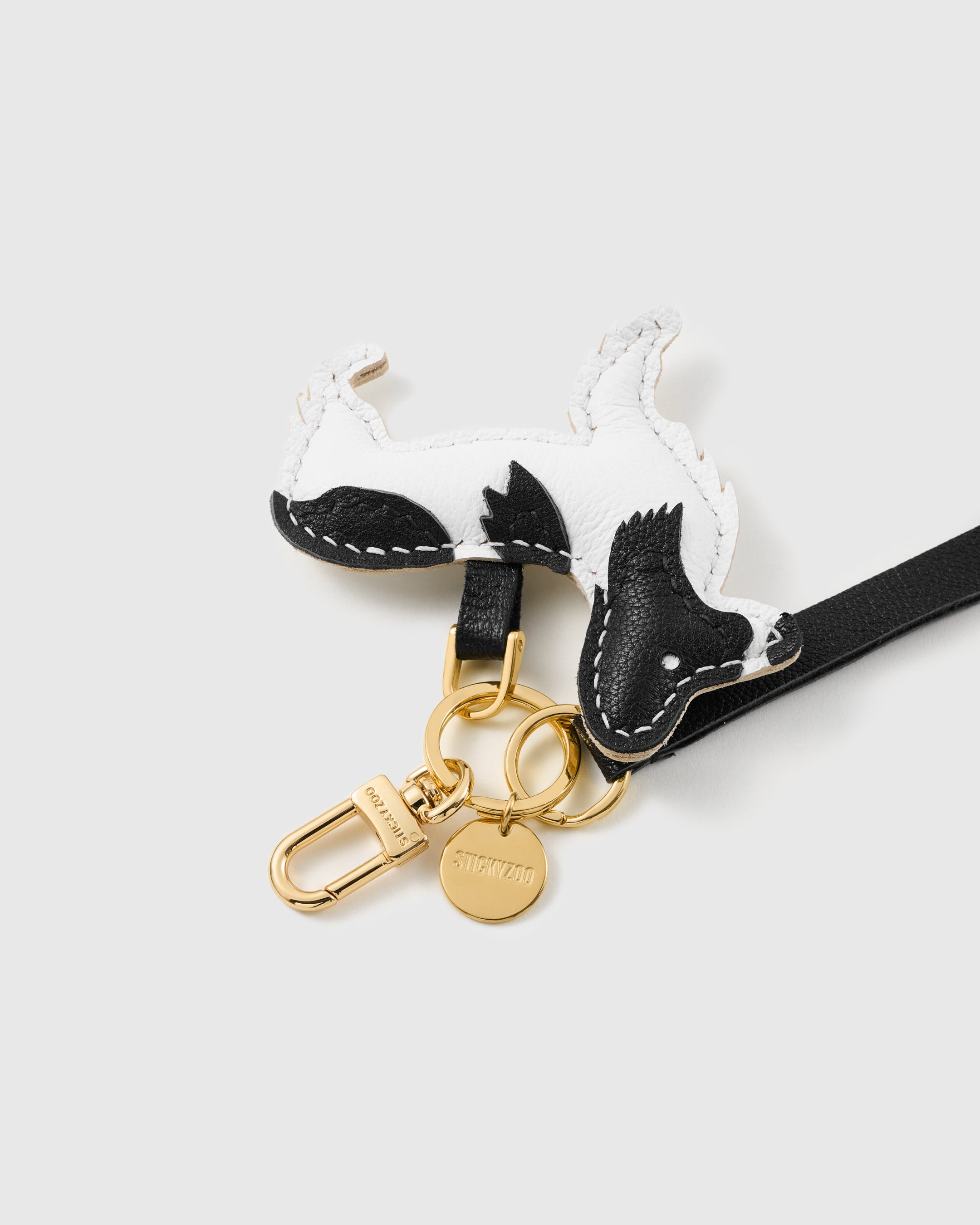 Close-up of the hand-stitched black-and-white leather dog charm and engraved STICKYZOO gold hardware