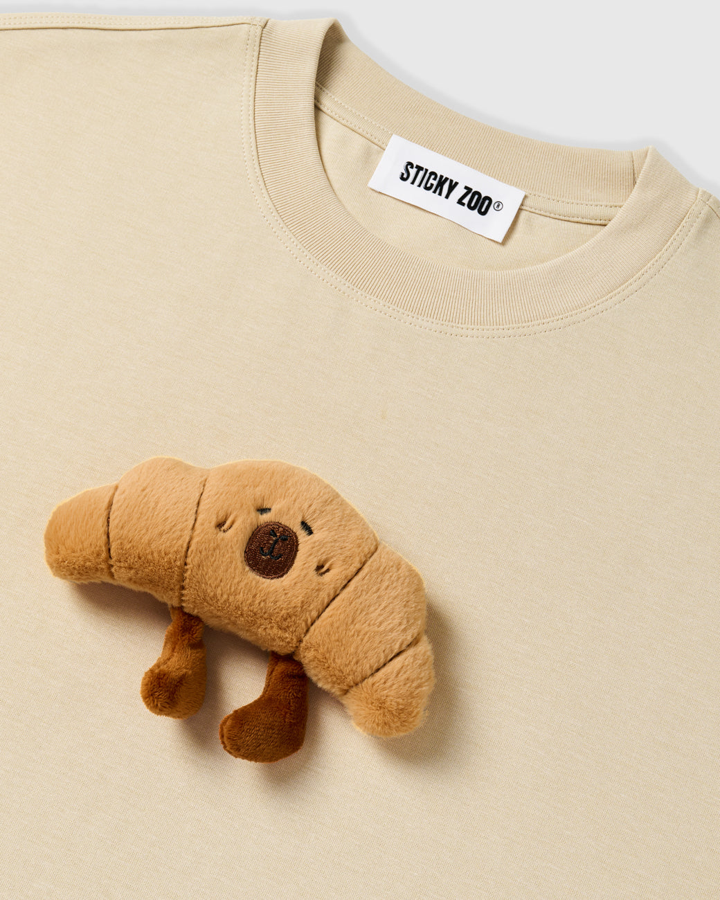 {{Rated 4.9 by thousands}} Detail of hand-stitched croissant applique on STICKYZOO beige t-shirt showing dimensional craft