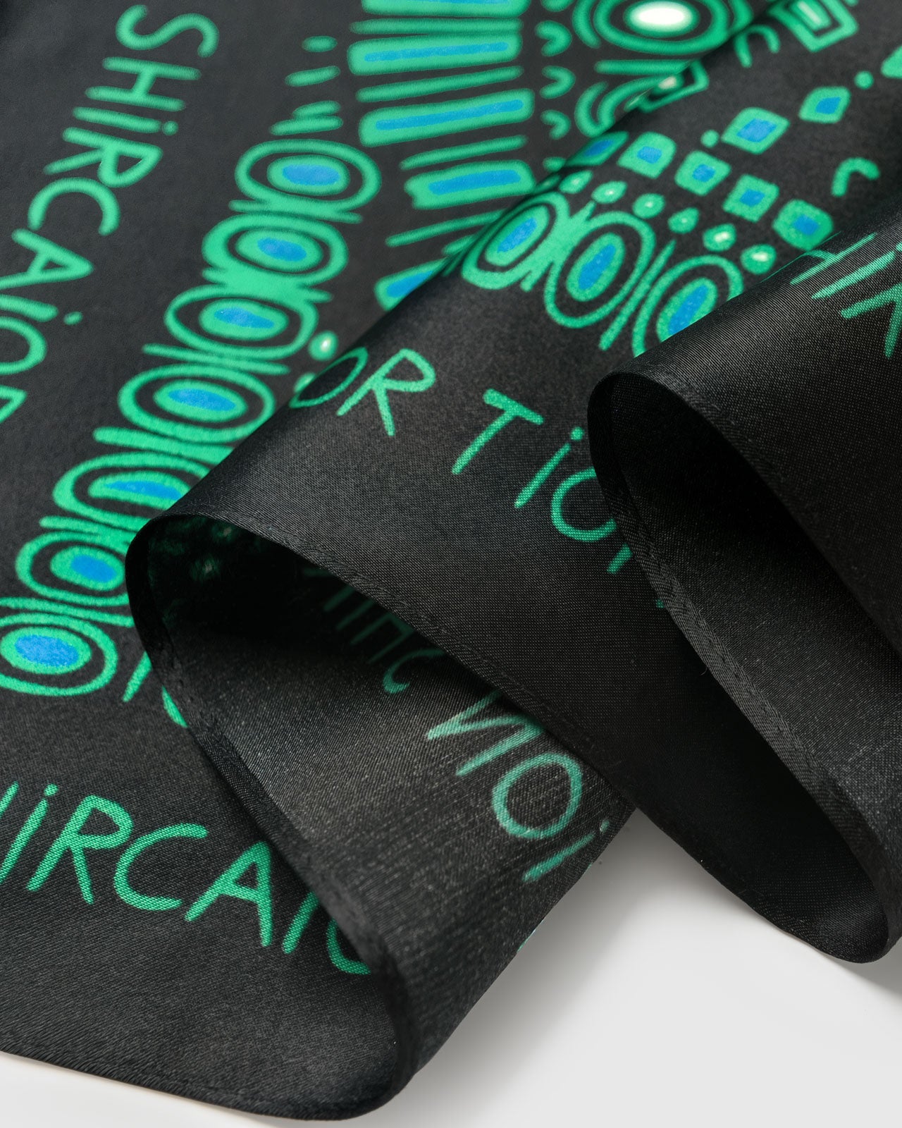 Close-up of the silk scarf border showing the deep black field and emerald lettering print on pure silk