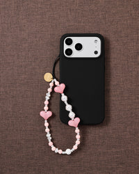 Bubblegum Heart beaded strap looped onto a black phone case on woven brown fabric, candy-pink hearts and pearl-effect beads on show.