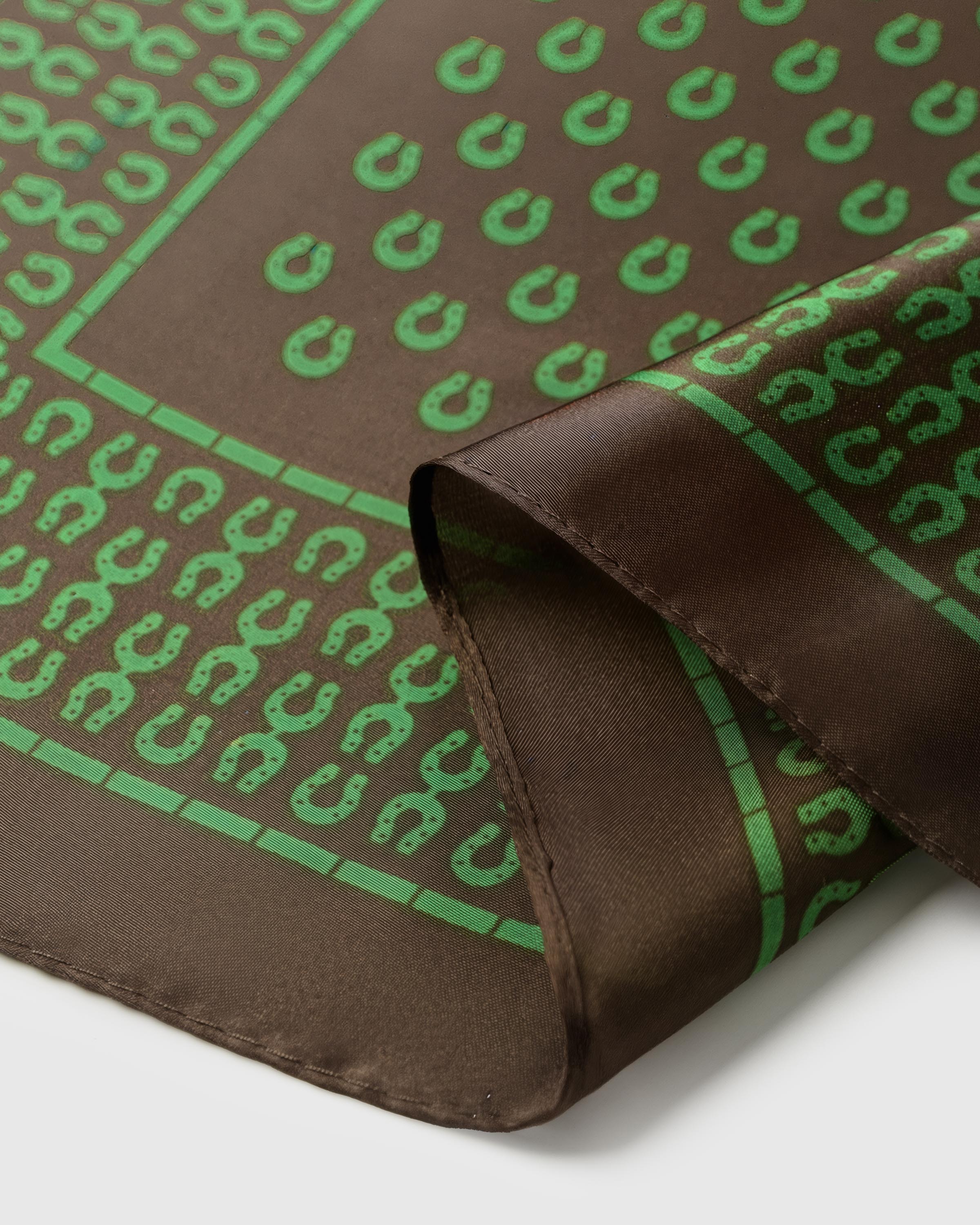 Close-up of the hand-illustrated green stirrup motif in archival ink on pure silk