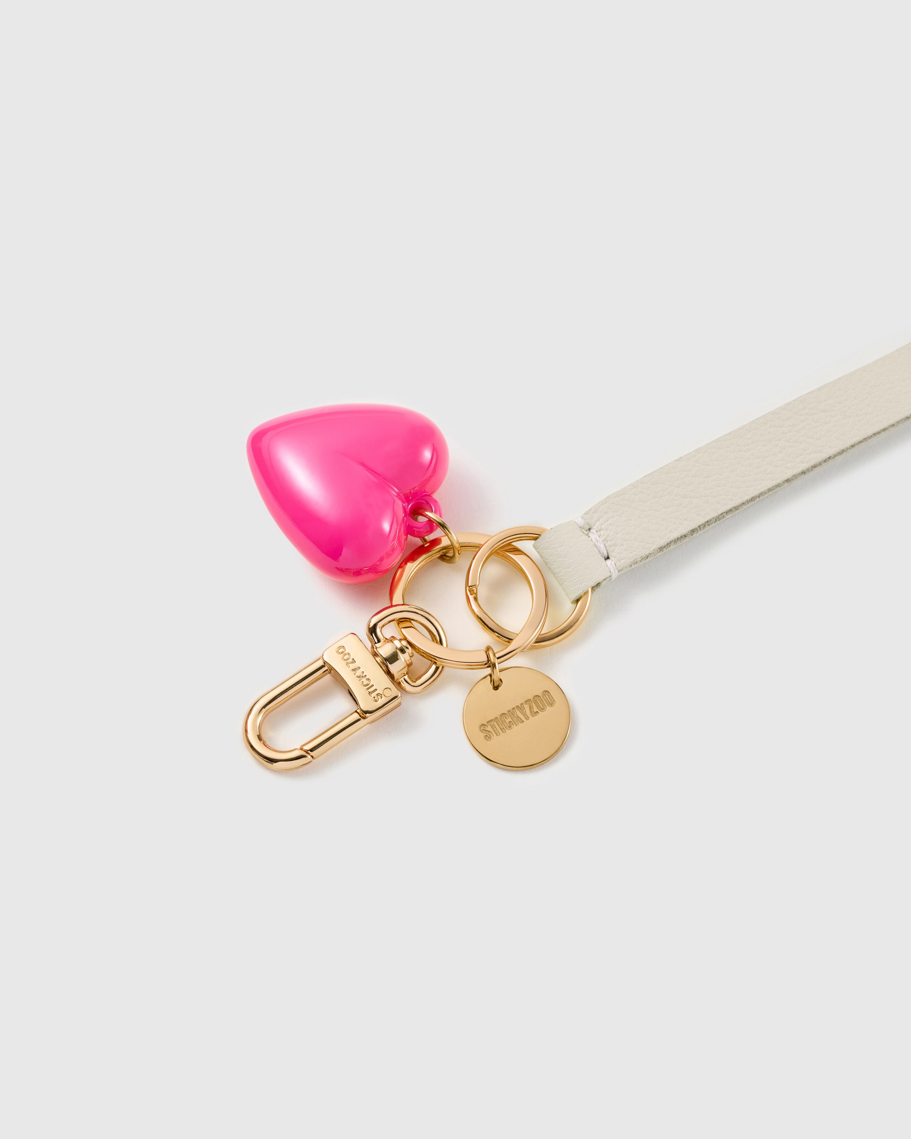 Ivory puff heart leather phone strap clipped to a phone case showing the hands-free wrist loop in use