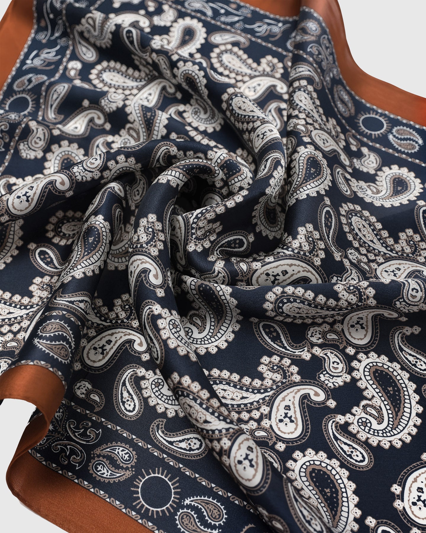 Close-up of the hand-illustrated paisley motif in ivory and pearl on the navy silk field