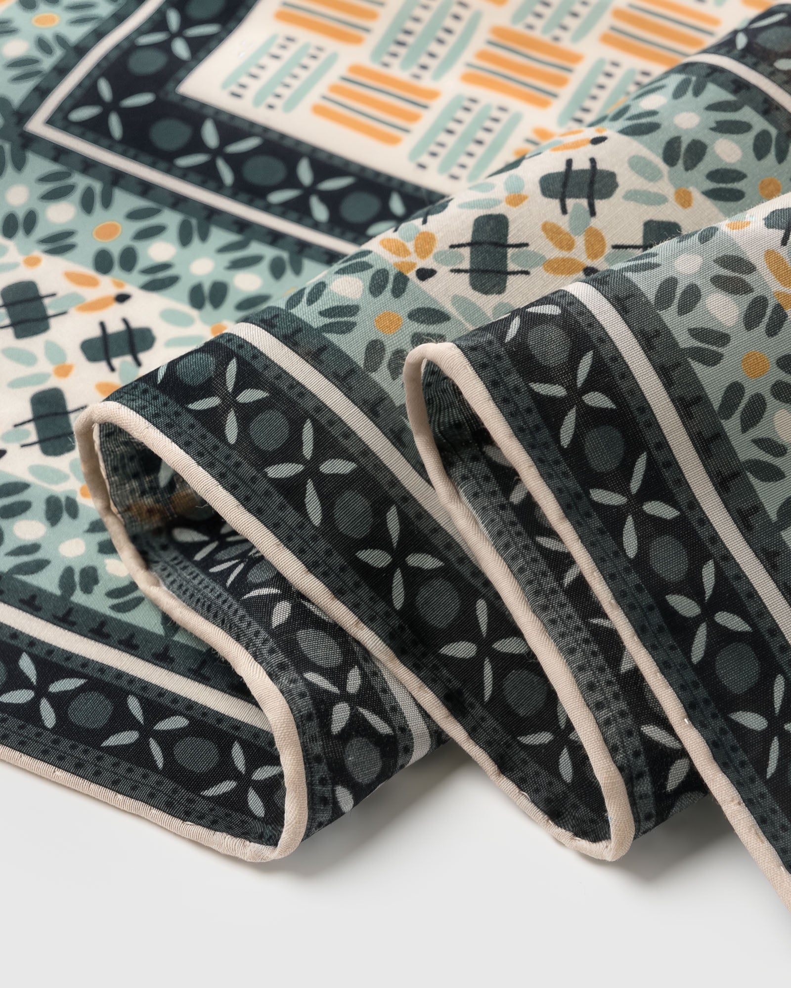 Edge detail of the mosaic silk scarf showing the tile-floret border on charcoal and cream margin