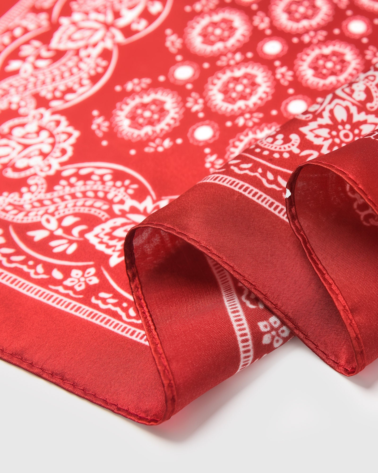 Edge detail of the rouge bandana silk scarf showing the floral border band and the silk finish