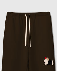 Close-up of hand-stitched plush dachshund with black coat and red apple on brown 350gsm cotton sweatpants showing 3D texture