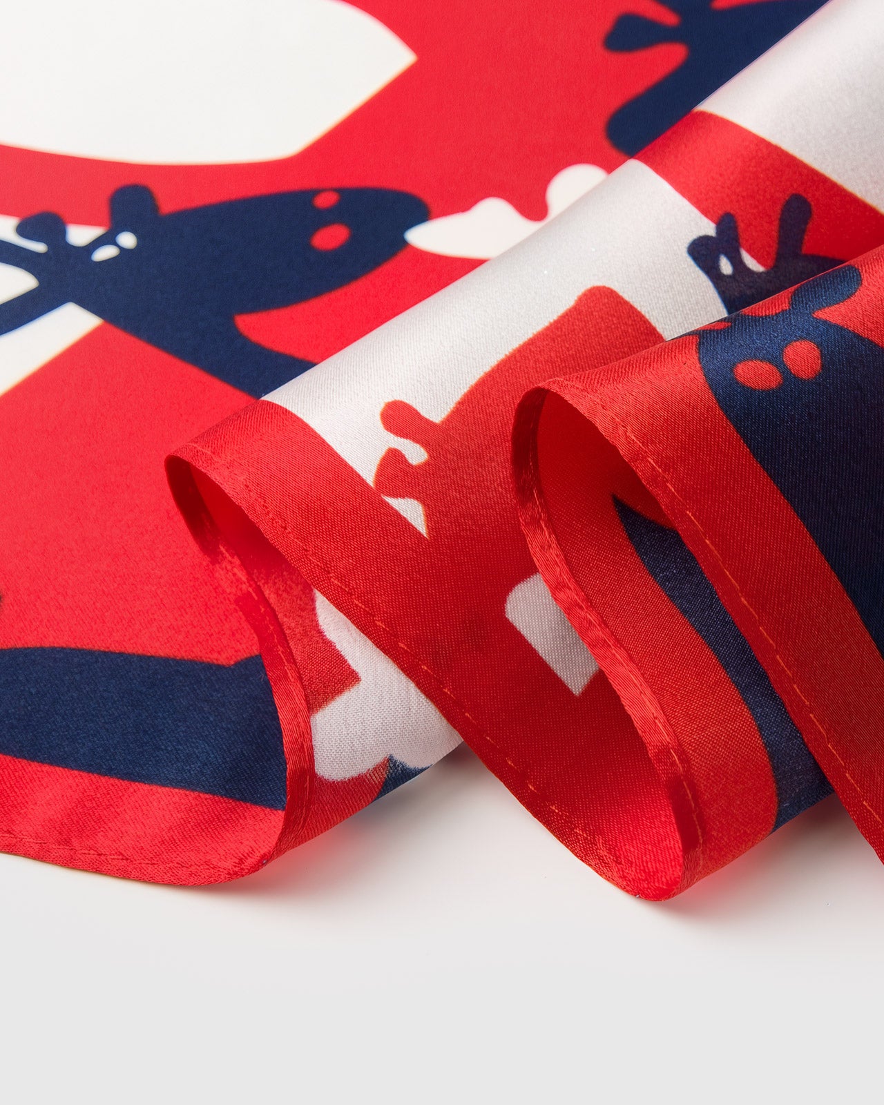 Close-up of the silk scarf showing the hand-illustrated red and navy giraffe silhouettes against ivory