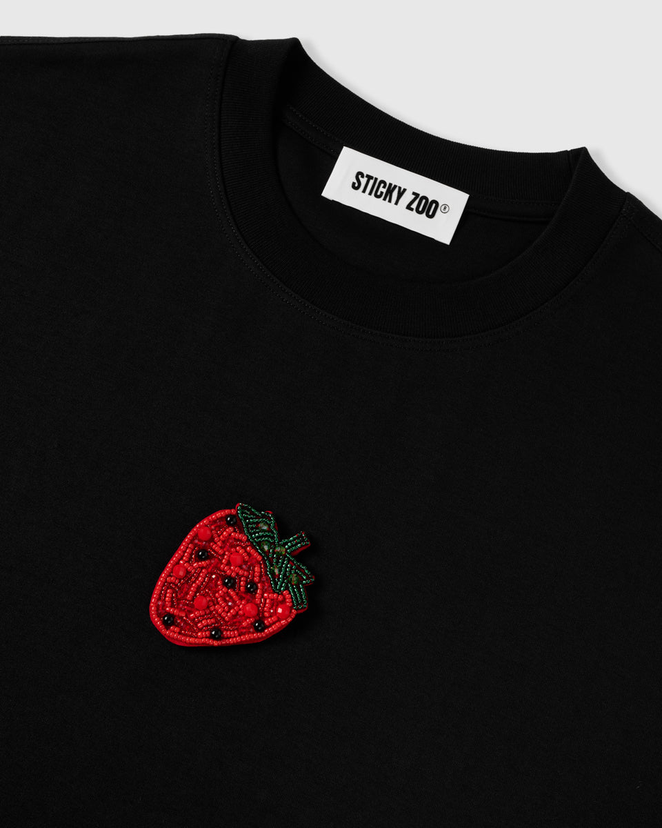 Macro of dense hand-sewn beadwork on the STICKYZOO Strawberry T-Shirt with the woven neck label, showing hundreds of individual glass beads.