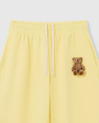 Close-up of hand-stitched plush teddy bear on lemon 450gsm cotton fleece showing dimensional 3D texture