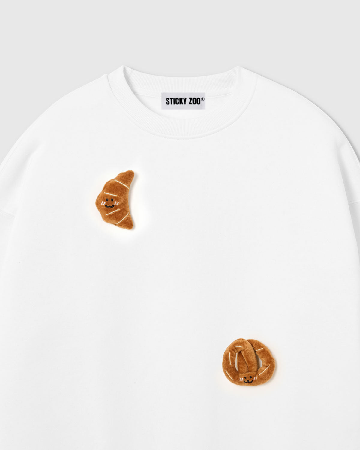 {{Touch it — real 3D plush}} Close-up of crescent plush croissant with smiley face on white cotton showing golden-brown layered texture