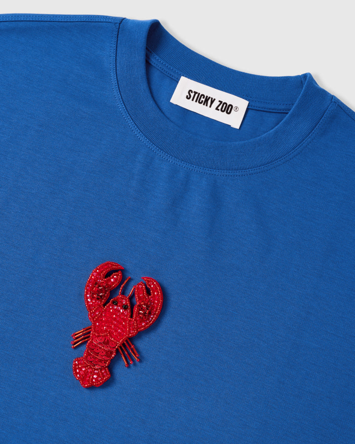 Detail of the beaded lobster applique beside the ribbed crew neck and STICKYZOO neck label, showing raised glass-bead and sequin texture.