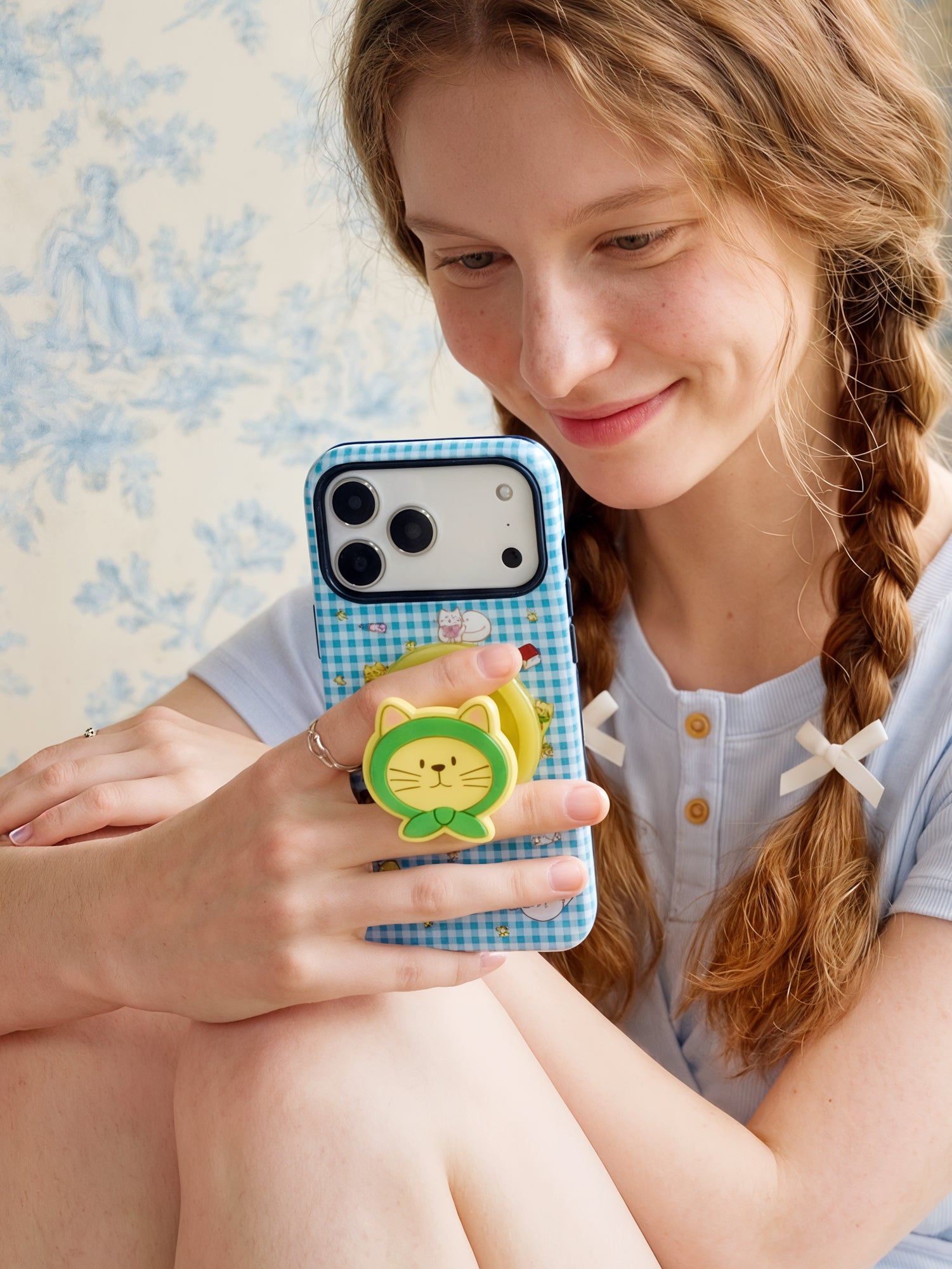 Phone held in hand with a finger through the retractable MagSafe grip on the back of the blue gingham case.